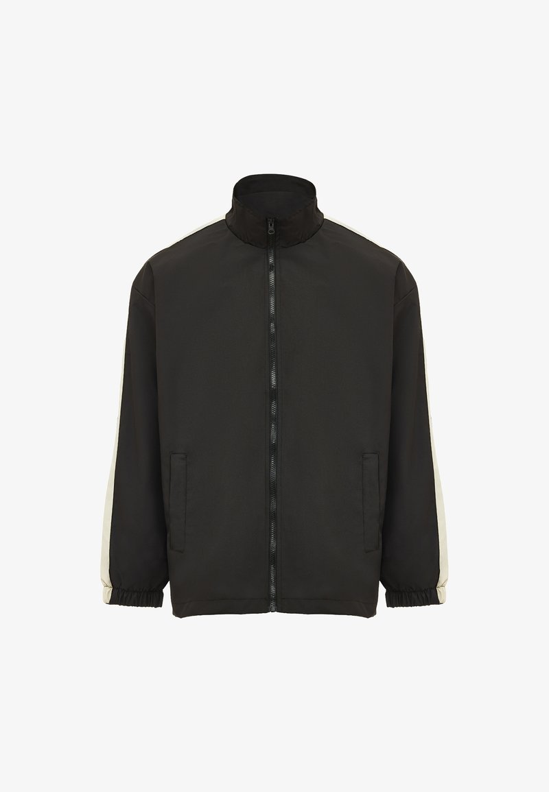 Sort jakke med høj krave, fuld lynlås foran og elatiske manchetter. Har cremefarvede striber langs ærmerne og foran lommerne.