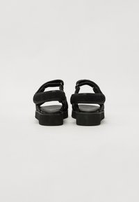 Svarte sandaler med to stropper, teksturert front og glatt såle. Har metalliske detaljer og en kraftig, teksturert gummisåle.