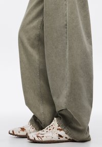 Pantalones anchos de color verde claro en tela suave; combinados con zapatos blancos con motas marrones y suela de goma texturizada.