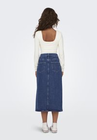 Long blue denim skirt with a straight cut and two back pockets, paired with a white long-sleeve top featuring a square back design.