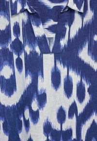 Niebiesko-biała tkanina w wzory, charakteryzująca się stylem tie-dye z abstrakcyjnymi kształtami i teksturowanym wełnianym splotem, z dekoltem w serek.