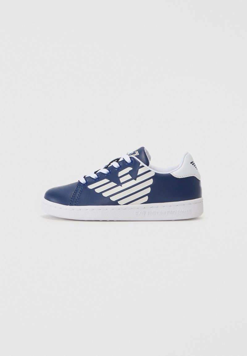 Baskets bleu marine avec lacets blancs, semelle blanche et grand logo d’aile blanche sur le côté sur fond uni.