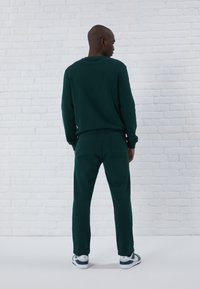 Mænds mørke grøn sweatshirt og matchende joggers, lavet af blødt stof med en afslappet pasform. Har et enkelt design og elastiske manchetter.