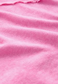 Tissu rose clair avec une surface douce et texturée. Le matériau semble léger et présente un motif côtelé subtil le long des plis.