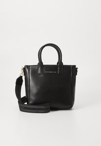 Sac à main en cuir noir avec deux courtes poignées et une bandoulière amovible. Détails de marque en ton doré à l'avant. Texture lisse, forme structurée.
