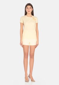 Top giallo chiaro a maniche corte con un dettaglio texturizzato e arricciato sulla spalla sinistra. Abbinato a pantaloni corti giallo chiaro coordinati.