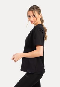 Zwart T-shirt met korte mouwen gemaakt van zachte stof, voorzien van een ontspannen pasvorm. Het ontwerp heeft een ronde halslijn en vlakke naden voor extra comfort.