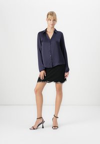 Navy blouse with a button-up front and long sleeves, paired with a black skirt featuring a scalloped hem and white accents. Strappy heels complete the look.