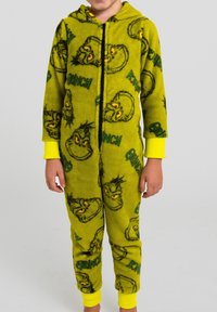 Tuta intera in pile verde con stampe del personaggio Grinch, dettagli gialli, chiusura con cerniera e cappuccio. Tessuto morbido e design giocoso.
