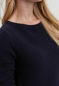 Pull en maille bleu marine avec un col rond et des manches longues, en tissu texturé et présentant des côtes visibles le long de l'ourlet.