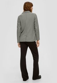 Karierte Blazer in Schwarz und Weiß mit Reverskragen, einem einzelnen Rückenschlitz und taillierter Passform, kombiniert mit schwarzen, schmalen Hosen.