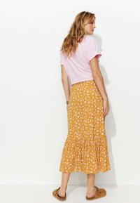 Jupe midi florale en moutarde avec un ourlet froncé, assortie à un top rose à manches courtes et des chaussures brunes à enfiler.