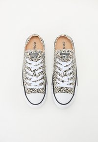 Tenisice od platna sa uzorkom leoparda, bijelim vezicama, gumeni đon i crnim detaljima. Imaju "Converse All Star" logo na jeziku.