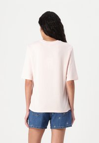 Lichtroze oversized t-shirt met korte mouwen, ronde halslijn, zachte textuur, gecombineerd met blauwe denim shorts met kleine patronen.