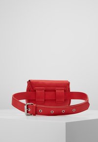 Punainen nahkavyölaukku jämäkällä muotoilulla, jossa on läpän sulkemismekanismi, kaksi etuhihnaa ja yhteensopiva säädettävä vyö hopeisilla yksityiskohdilla.