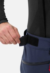 Sac en tissu bleu marine avec une fermeture à velcro. Il dispose d'une poche zippée et de sangles réglables. Texture lisse avec des détails de couture visibles.