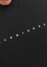 Zwarte katoenen t-shirt met witte tekst "KICK & JONES" in een modern lettertype over de borst. Korte mouwen, ronde hals ontwerp.