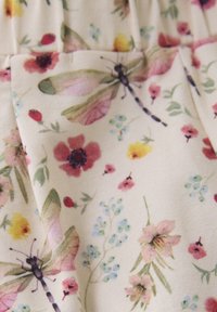 Blomstret stof med en cremefarvet baggrund og farverige blomster samt guldsmededesign i nuancer af pink, blå og gul. Glat tekstur.