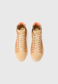 Sneaker alte in suede beige, con una parte frontale liscia, lacci bianchi e un colletto imbottito arancione. Finiture nere e suola testurizzata.