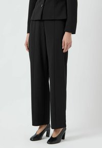 Černé přizpůsobené kalhoty vyrobené ze strukturované tkaniny, charakterizované rovně střiženými nohavicemi, bočními kapsami a hladkou texturou. V kombinaci s černými podpatekmi.