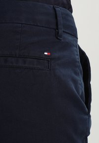 Tmavě modré bavlněné kalhoty s hladkou texturou, na zadní kapse s malým logem značky v červené, bílé a modré barvě.