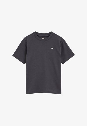 Tmavohnedé tričko s krátkym rukávom vyrobené z mäkkej tkaniny, s okrúhlym výstrihom a malým bielym logom vtáka na ľavej strane hrude.