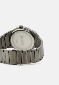 Reloj de acero inoxidable con un acabado gris, que presenta un diseño de pulsera de eslabones. La parte posterior muestra el logo "BOSS" y una caja circular y suave.