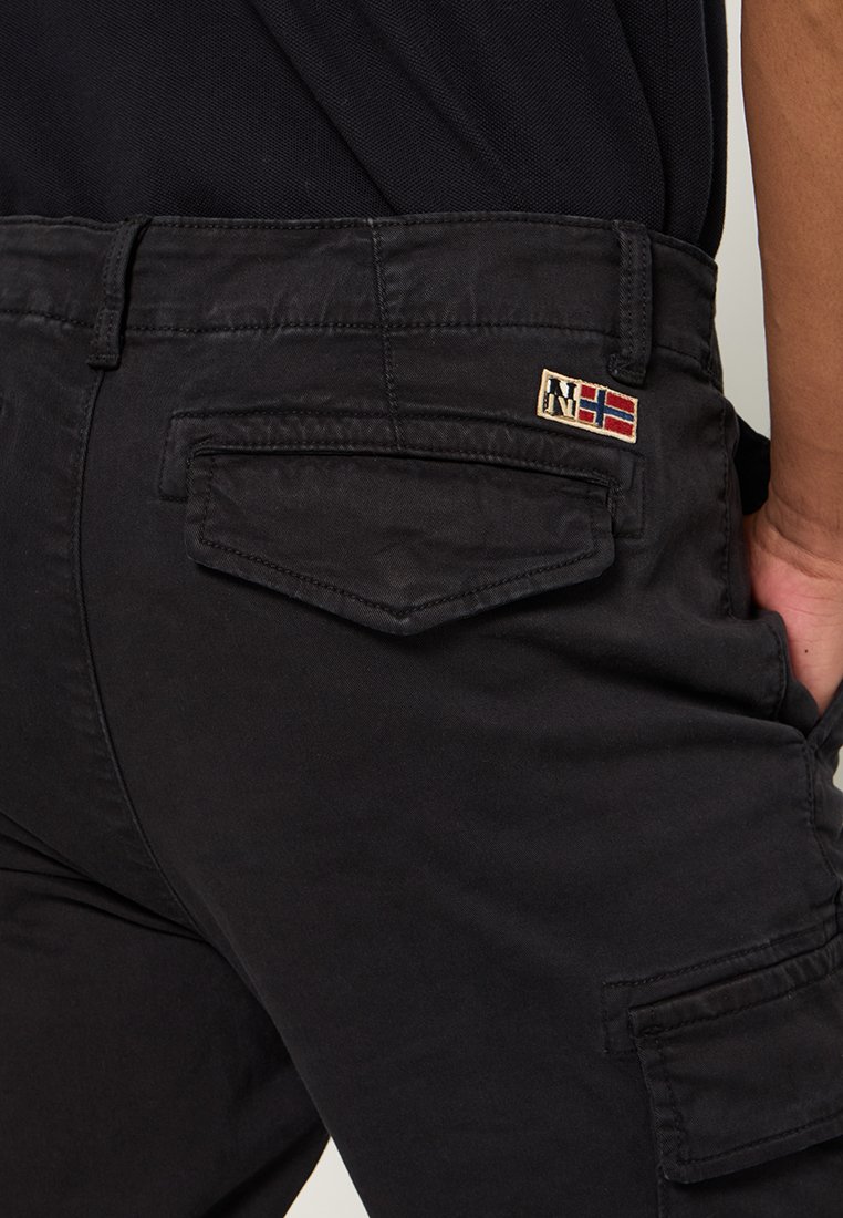 Pantalones cargo negros de mezcla de algodón, con un bolsillo trasero con solapa, costuras visibles y un parche con un emblema y detalle de bandera.