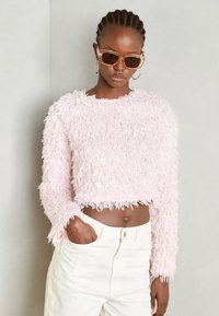 Helles rosa, flauschiges Crop-Pullover mit geripptem Saum und langen Ärmeln, kombiniert mit hochgeschnittenen weißen Hosen. Besteht aus strukturiertem, weichem Material.