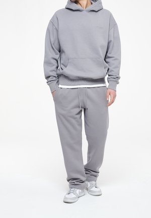 Grauer Hoodie und passende Sweatpants aus weichem Baumwollmaterial mit lockerer Passform. Mit einer Fronttasche und einem Kordelzugbund. Sneaker runden den Look ab.