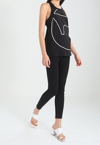 Svart linne med vitt geometriskt mönster, kombinerat med svarta skinny jeans och vita blockklackade sandaler. Slät väv, figurnära passform.