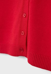 Približek rdeče pletene tkanine s tremi rdečimi gumbi in rebrasto obrobo na oblačilu.