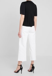 Svart topp med korta ärmar tillsammans med vita jeans med vida ben och rå kant, samt svarta högklackade sandaler med remmar runt ankeln.