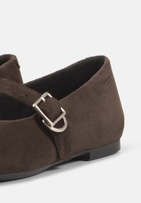 Scarpa in suede marrone con suola piatta, punta rotonda e cinturino regolabile con fibbia in metallo argentato. Texture liscia, design classico.