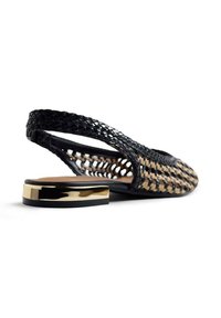 Zapato plano negro tejido con talón en bandolera, tacón bajo metálico dorado y lados abiertos, exhibido sobre fondo blanco.