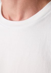 Weißes Baumwoll-T-Shirt mit Rundhalsausschnitt und leichter Textur. Zeigt feine Rippung am Kragen mit subtilen Nähdetail.