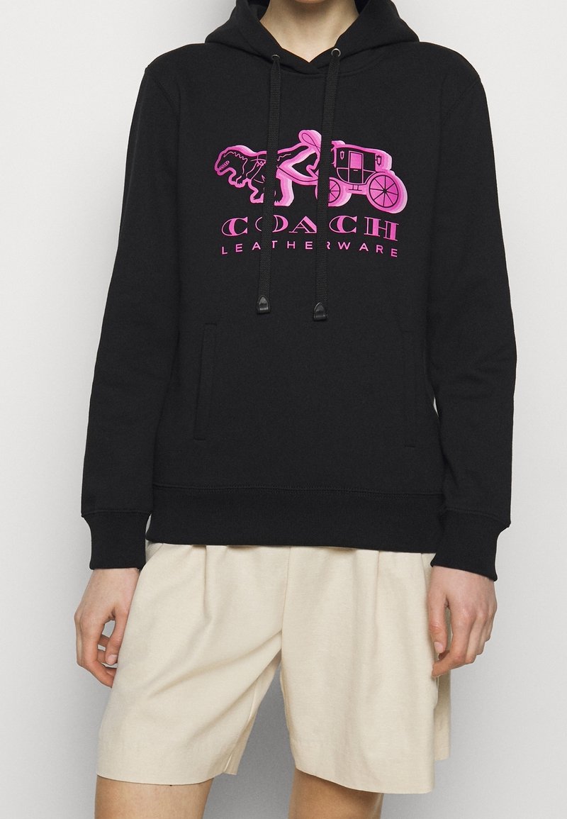 Sudadera negra con capucha que presenta un logo gráfico en rosa de un caballo y carruaje con el texto "COACH LEATHERWARE", hecha de un tejido suave y con un bolsillo frontal.