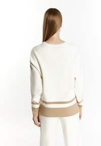 White knit sweater with long sleeves, featuring a round neckline and horizontal beige and white stripes along the cuffs and hem.