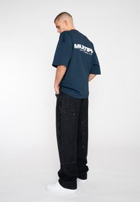 Dunkelblauses oversized T-Shirt mit weißem grafischem Text auf der Rückseite, kombiniert mit lässigen schwarzen Jeans und weißen Sneakern.