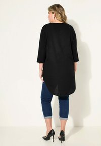 Túnica negra con dobladillo curvado, mangas tres cuartos, combinada con jeans azules con dobladillos y tacones altos negros. Textura suave, diseño casual.