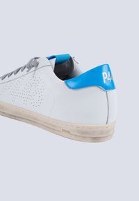 Weiße Leder-Sneaker mit grauen Schnürsenkeln, blauer Fersenlasche und perforiertem Design an der Seite. Abgenutzte Sohle zeigt leichte Verschmutzungen und Textur.
