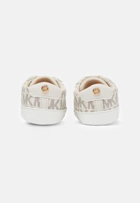 Zapatillas en beige claro con una cubierta de malla estampada. Presentan una suela de goma blanca y un logotipo dorado en el talón.