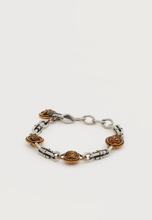 Bracelet chaîne en argent avec quatre médaillons en or ornés d'un motif tête de lion, reliés par des connecteurs en argent détaillés, sur fond blanc.