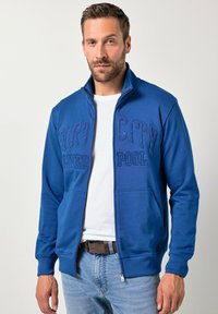 Sudadera azul con cremallera y la inscripción "PORT CITY LIVERPOOL" en letras con textura. Cuenta con mangas largas, cuello alto y bolsillos laterales.