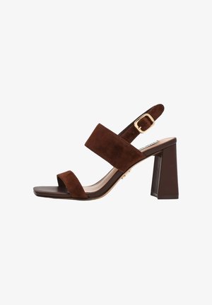 Sandalo aperto in pelle scamosciata marrone con ampie fasce, fibbia dorata regolabile e tacco largo a blocco su sfondo bianco.