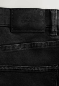 Black denim jeans with a leather tag labeled "NEXT SIGNATURE." Features include a smooth texture, single back pocket, and clean stitching.