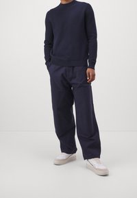 Mörkblå stickad tröja med rund halsringning, tillsammans med löst sittande mörkblå cargobyxor och vita sneakers. Mjuk textur och avslappnad design.