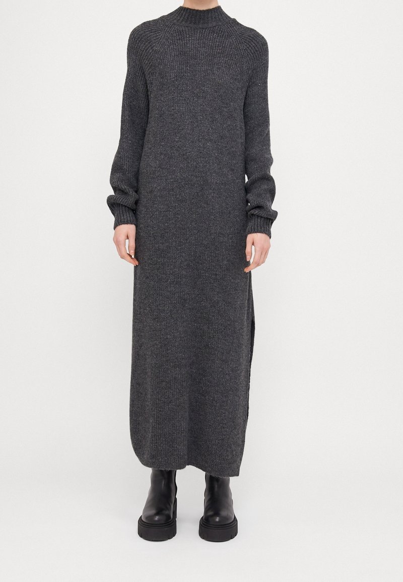 Robe longue en maille gris foncé avec col montant, texture côtelée et manches longues ; dotée de fentes latérales. Associée à des bottines à plateforme noires.