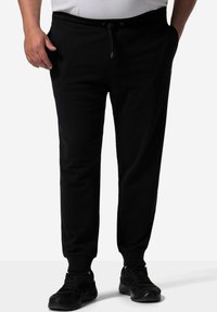 Zwarte trainingsbroek van een zachte, rekbare stof. Bevat een elastische tailleband met een trekkoord en ribborstels aan de enkels.