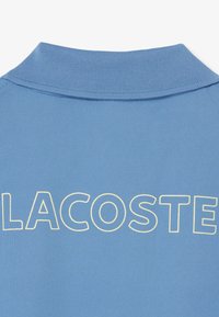 Blauw stoffen poloshirt achterkant met geribde kraag en grote omlijnde tekst "LACOSTE" in lichtgeel over de bovenrug.